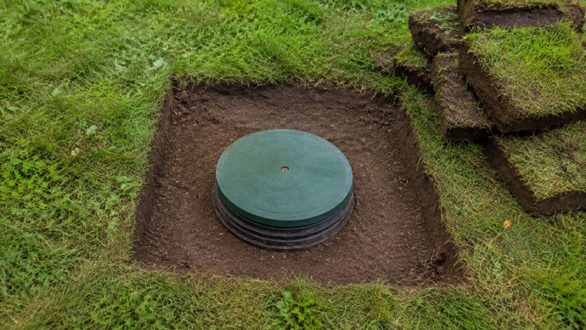 Green septic tank riser lid exposed in a neatly cut residential lawn