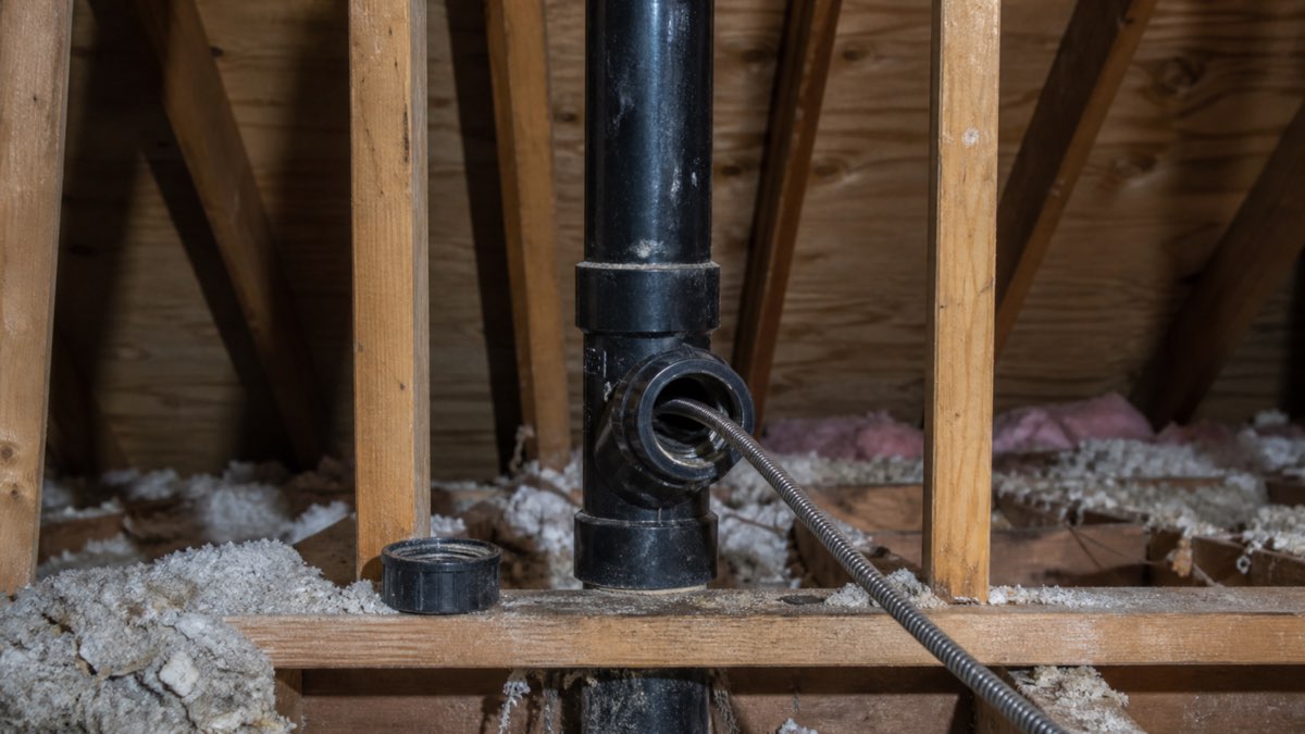 Drain auger cable inserted through an indoor cleanout on an attic vent stack