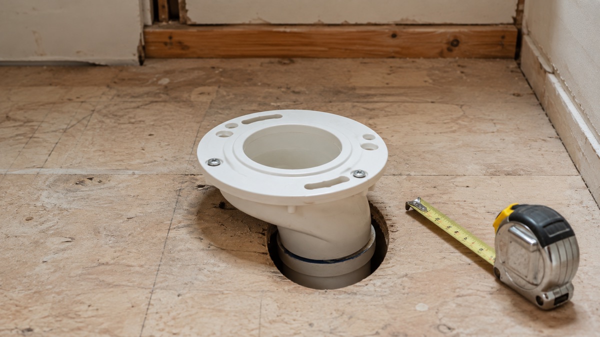 Offset toilet flange installed over a bathroom subfloor drain beside a tape measure.