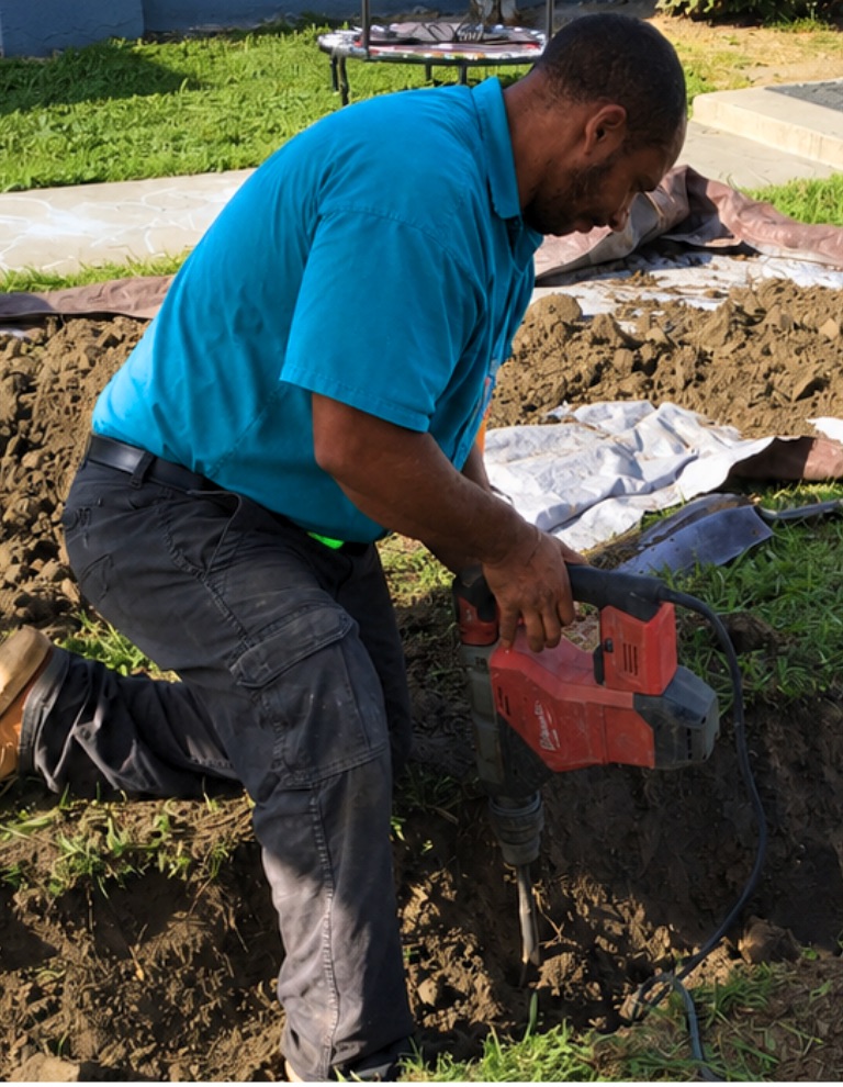 Elite Rooter technician excavating a sewer trench with the lawn protected by tarps