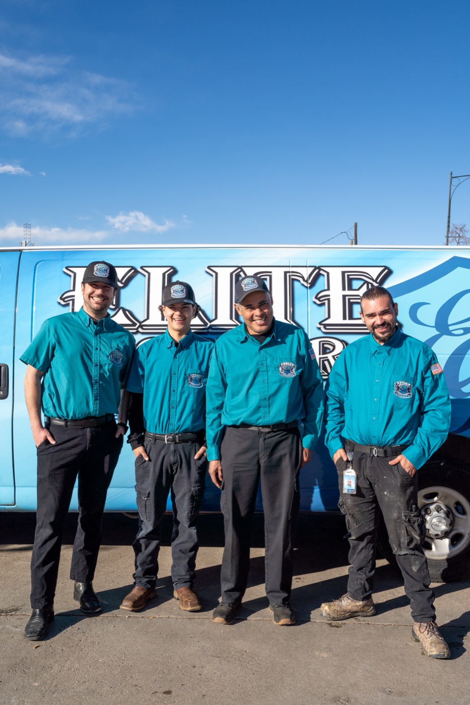 Four Elite Rooter plumbing technicians standing together beside a service van